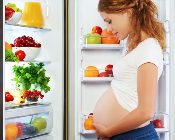 41614113 - nutrition and diet during pregnancy. pregnant woman standing near refrigerator with fruits and vegetables